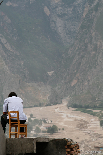 坐在房顶上，远远望着对面泥石流横扫过的家园